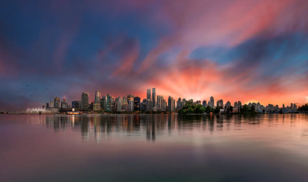 Downtown Vancouver towers glowing across the water under a dramatic sunset